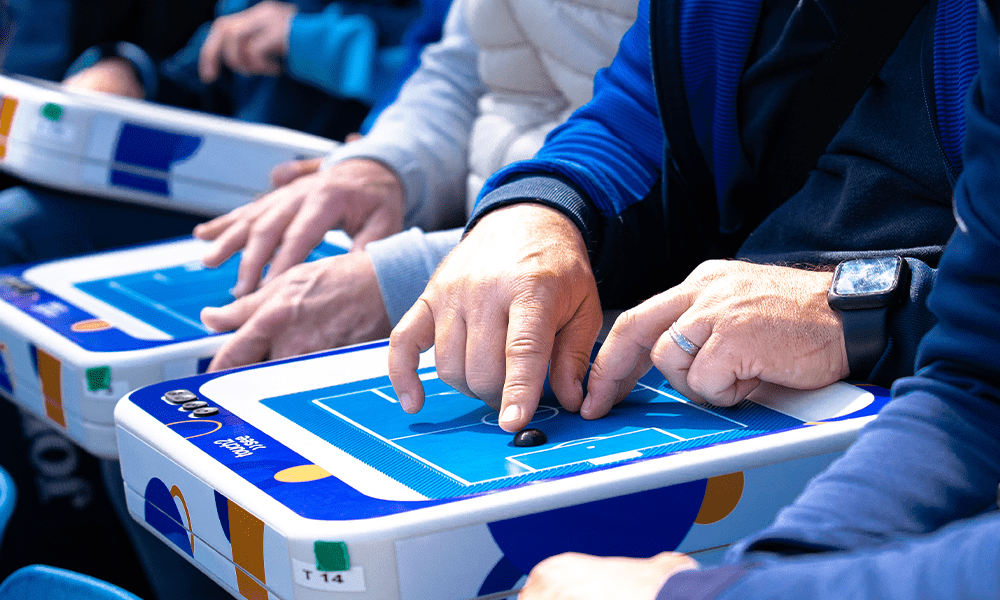 Several individuals seated with touch2see tablets in their hands during a sports match.