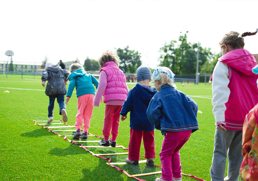 Children playing a stepping game on a grassy field at school.