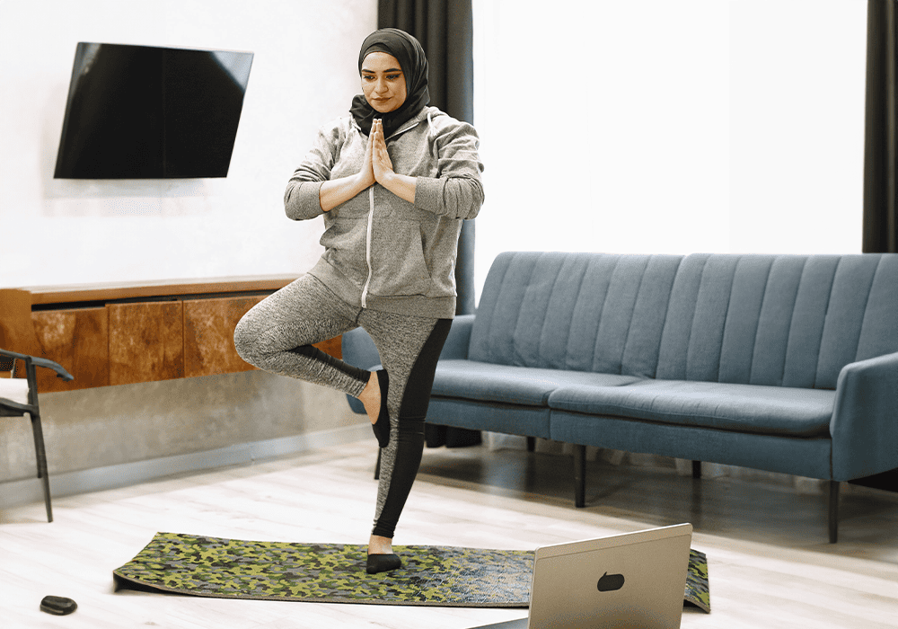 Person practicing yoga at home with a laptop.